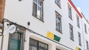 A white building with a red roof and multiple windows. There is a green door and a sign that reads "SUBWAY".