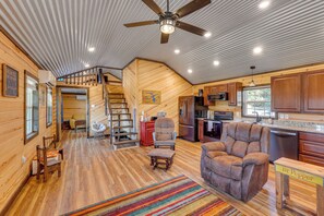 Un intérieur de cabine spacieux, avec un plancher en bois, un grand fauteuil en cuir marron, un coin repas et une cuisine dotée de meubles en bois.