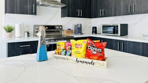 A modern kitchen with dark cabinets, a marble countertop, a gas stove, a microwave, and a bowl of snacks. - Spacious 4BR Niagara Family Home•Near Falls, Brock & Wine Country •Free Parking. (Thorold)