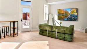 A modern living room with a green sofa, a dining table with stools, and a large painting on the wall. - Gallery Flat by Dupont Circle Large patio & Grill (Washington)