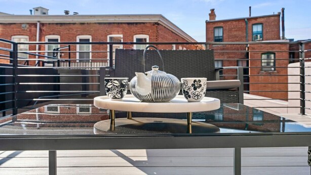A glass-top table with a white teapot and two patterned cups on a balcony with a view of brick buildings. - Gallery Flat by Dupont Circle Large patio & Grill (Washington)