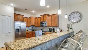 A kitchen with wooden cabinets, stainless steel appliances, a granite countertop, and bar seating. - ChampionsGate Resort Perks! Fun-Filled Family Home (Davenport)