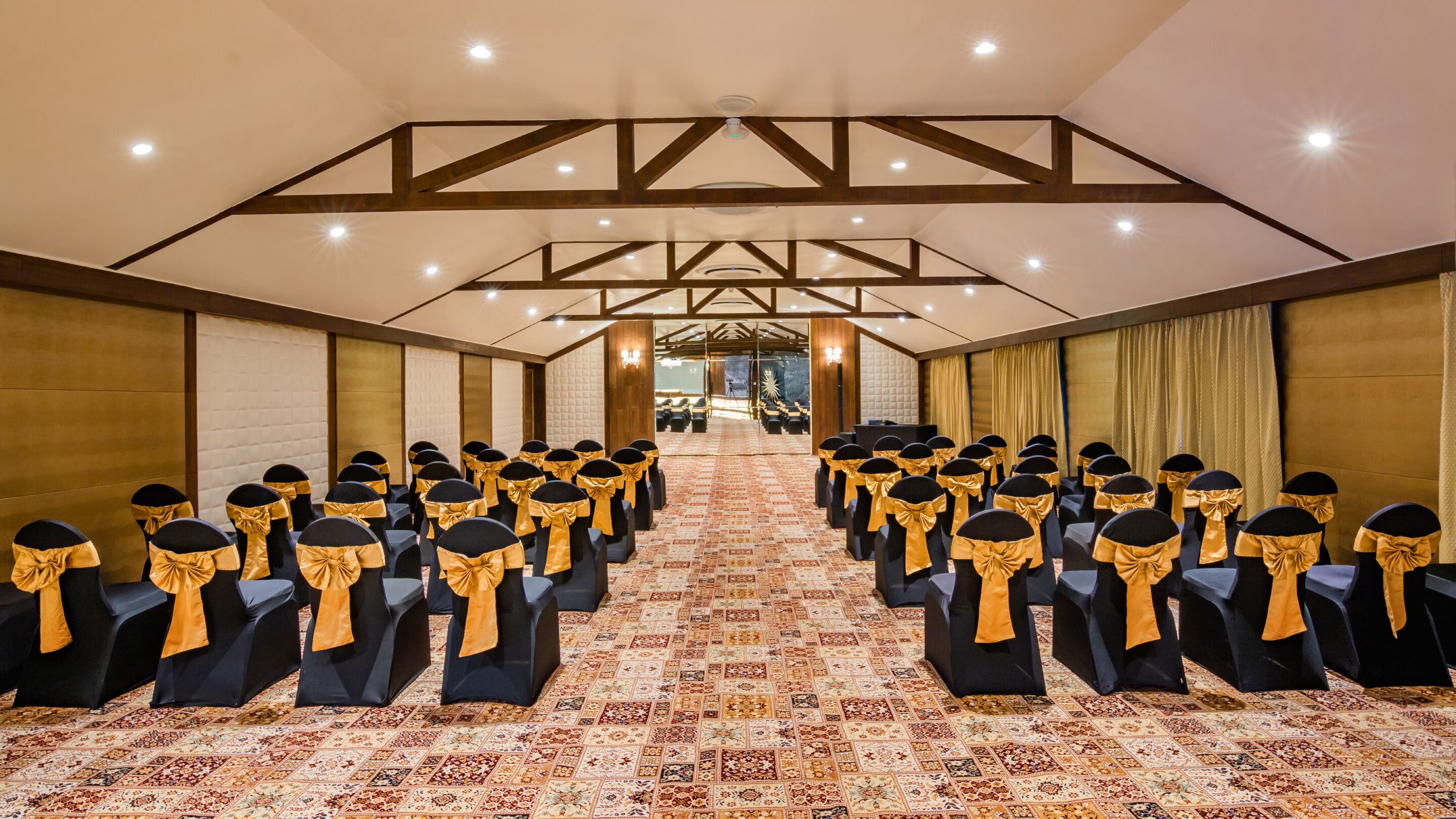 Un salón de conferencias con filas de sillas, una alfombra estampada y vigas de madera en el techo.