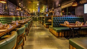 Een restaurant met groen gestoffeerde zitbanken en houten tafels, met een lange balie en een muurschildering.