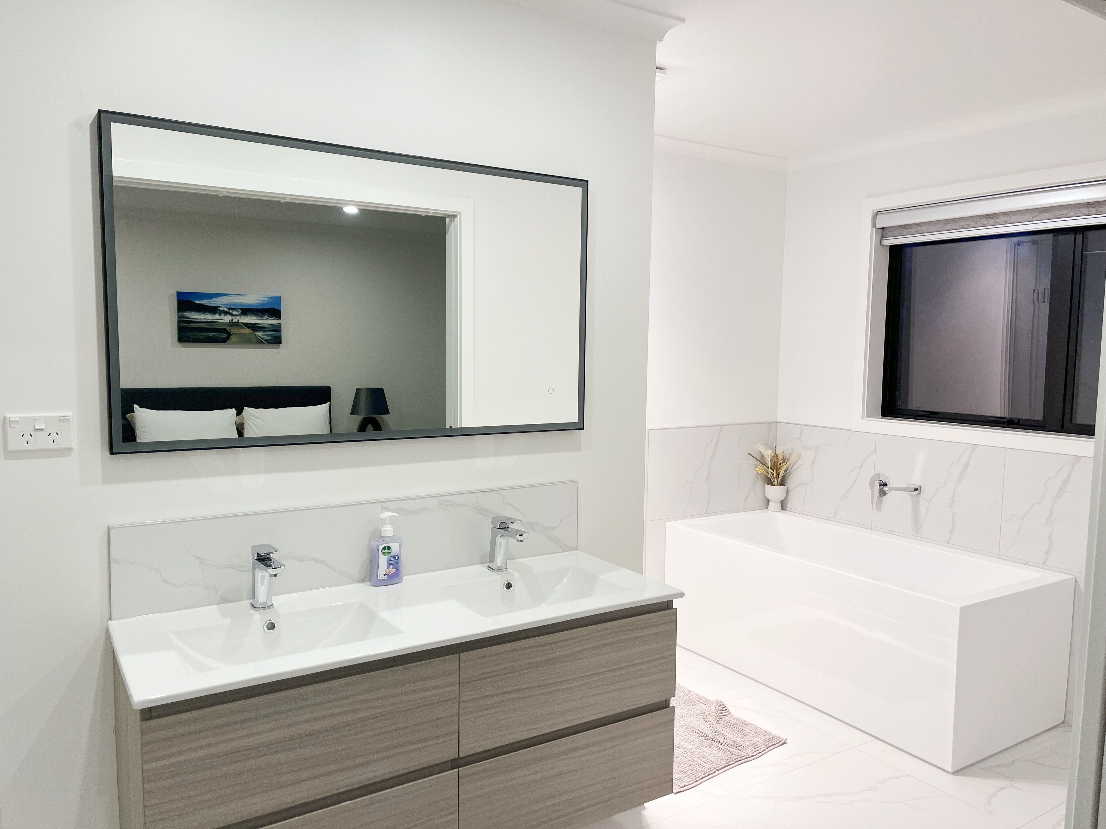 A modern bathroom with a large mirror, two sinks, a vanity, and a bathtub.