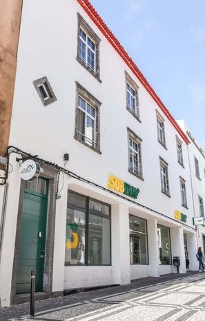 Un bâtiment à la façade blanche, au toit rouge et aux nombreuses fenêtres. On y trouve une devanture avec une porte verte et une enseigne sur laquelle on peut lire « SUBTOWN ».