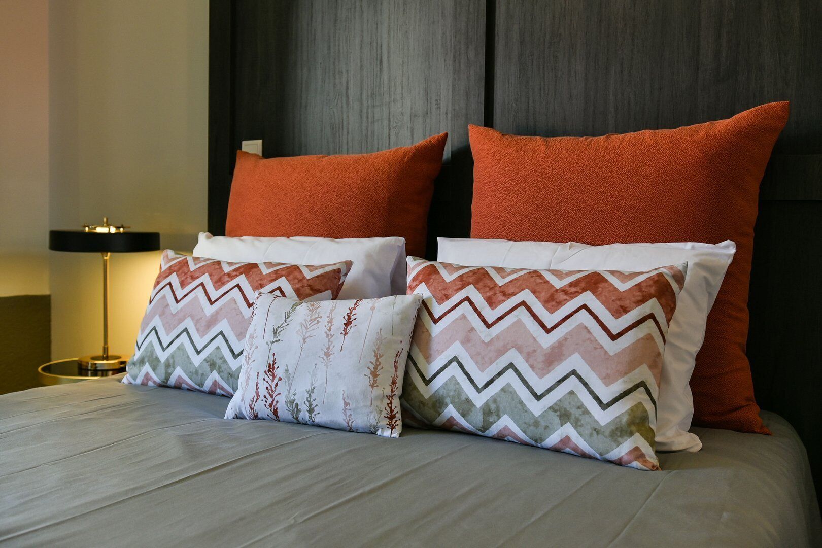 A bed with two large orange pillows and two smaller patterned pillows.
