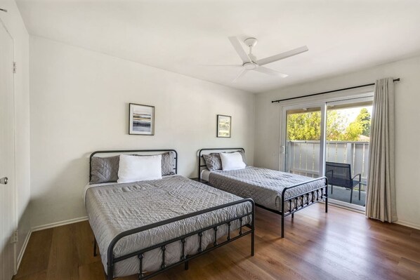 A room with two beds, a ceiling fan, and a balcony with a chair. - Monthly Rental Near South Coast Plaza | 1Bed1Bath (Santa Ana)