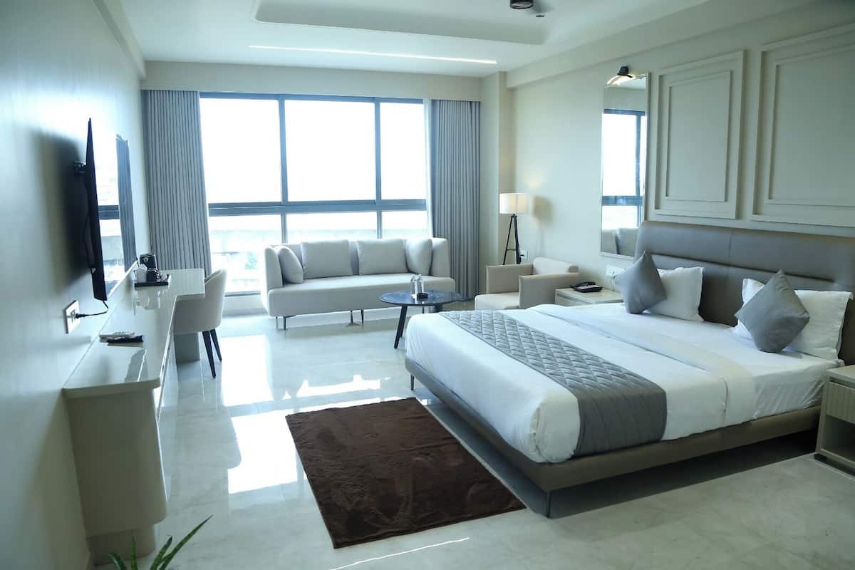 A modern hotel room with a large bed, a sofa, a desk, and a TV.