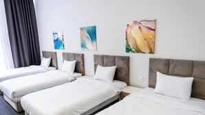 Une chambre d’hôtel avec trois lits simples, chacun doté d’une tête de lit grise et de linge de lit blanc. Trois tableaux abstraits ornent le mur.