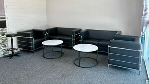 A corner room with a black leather sofa, two white round tables, and a small black bar stool. - Gemilang Star Hotel (Port Dickson)