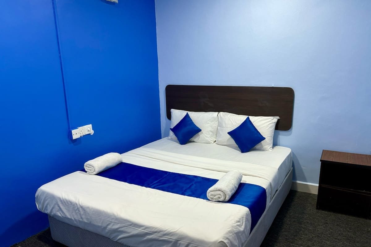 Una cama individual con una colcha blanca y azul, dos almohadas azules y un cabecero de madera.