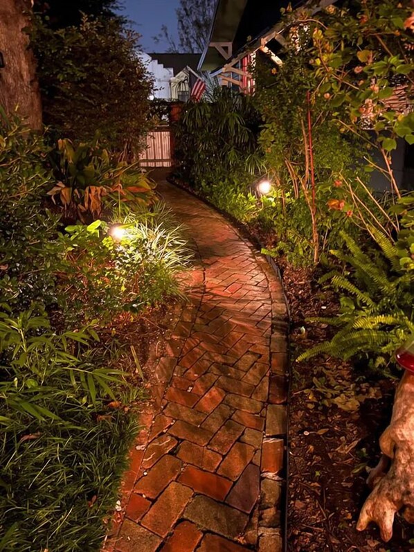 Un sendero de ladrillo que atraviesa un jardín con diversas plantas y árboles.