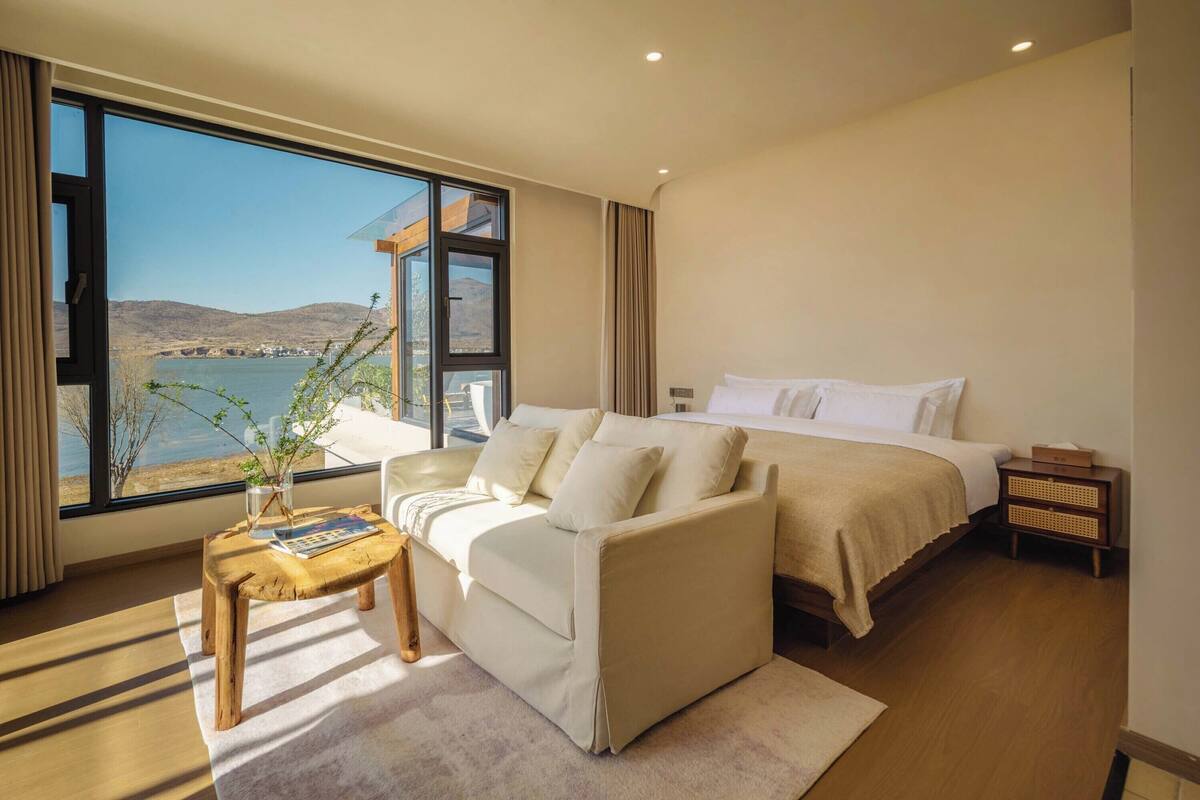 Une chambre à coucher comprenant un lit, un canapé, une table de chevet et une fenêtre donnant sur un plan d’eau et des collines.