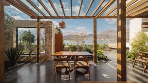 A covered patio with a wooden table and chairs, stone walls, and a view of the mountains and lake. - Dali Antu Yuanchu seaview Homestay (Dali)