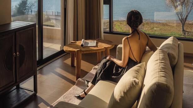 A modern room with a large window offering a view of a lake and hills. There is a sofa and a small wooden table with a book on it. - Dali Antu Yuanchu seaview Homestay (Dali)