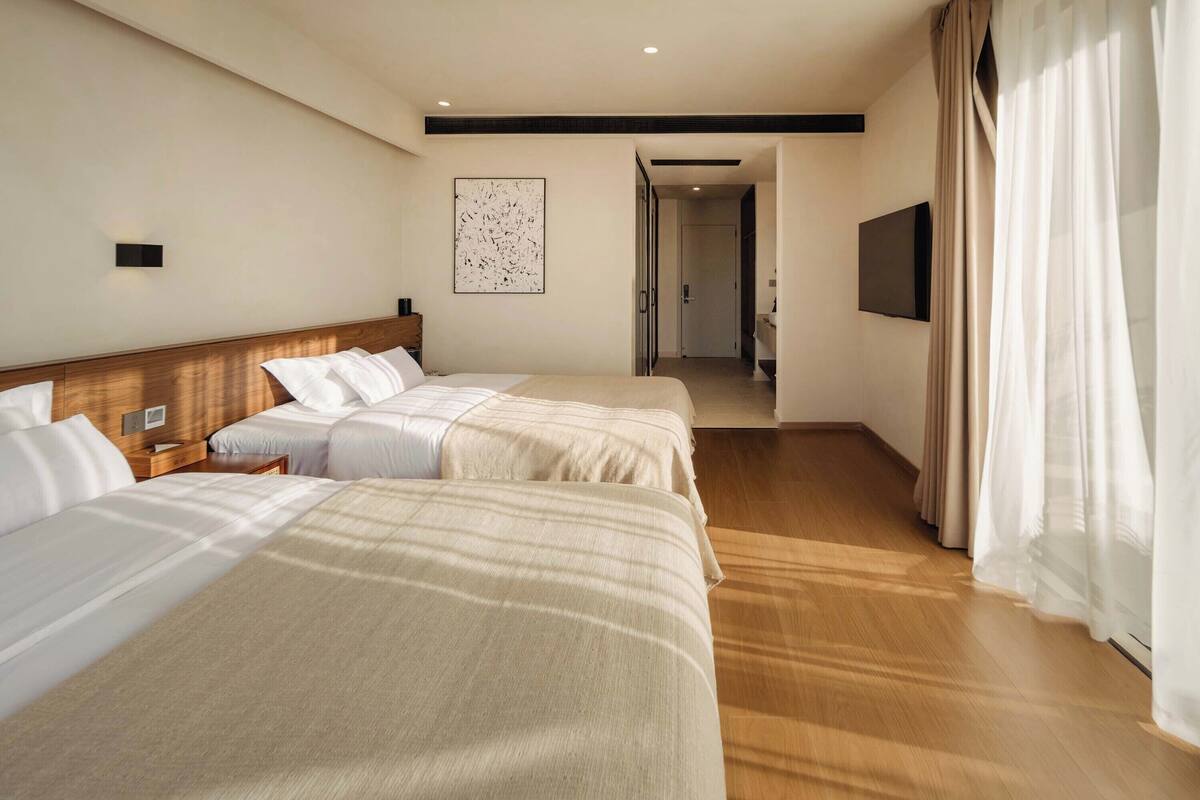 Une chambre d’hôtel avec deux lits, un téléviseur à écran plat, un tableau au mur et un plancher en bois.