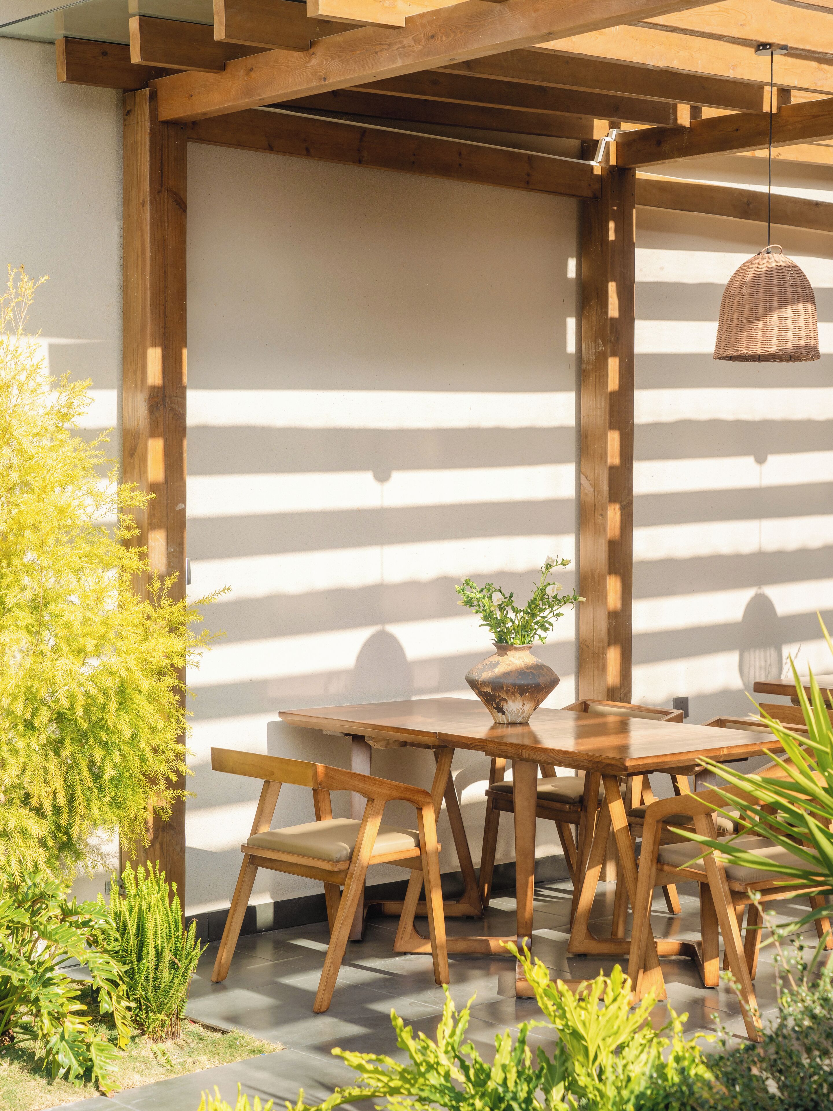 A wooden pergola with a table and chairs underneath, surrounded by greenery.