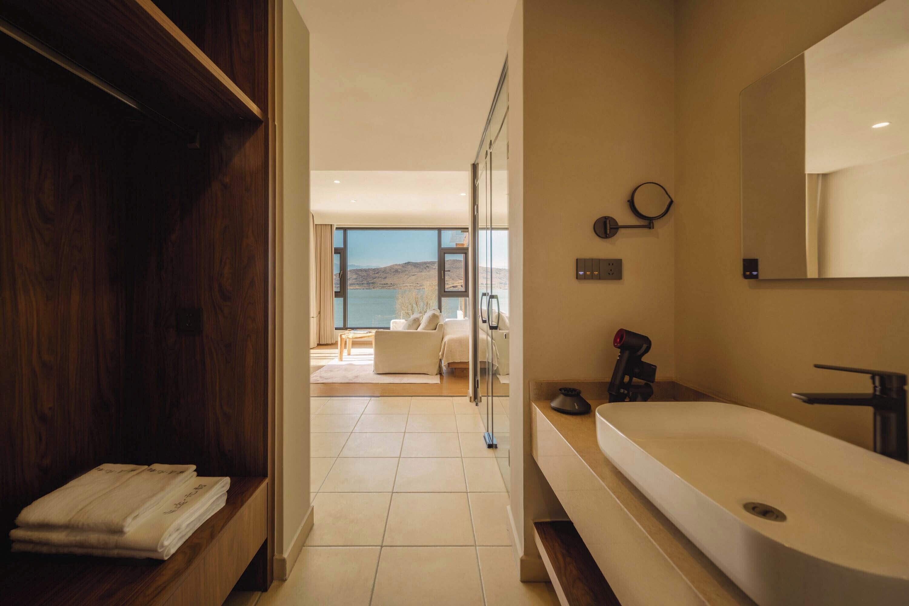Casa de banho moderna com uma banheira grande, um espelho e vista para uma sala de estar com sofá e uma janela ampla.