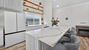 A modern kitchen with white cabinetry, a marble island, and a built-in seating area. - Upscale Retreat-Games, Comfort & Cozy Vibes Await! (Houston)