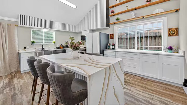 A modern kitchen with a marble island, bar stools, and built-in shelves. - Upscale Retreat-Games, Comfort & Cozy Vibes Await! (Houston)