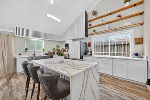 A modern kitchen with a marble island, bar stools, and built-in shelves.