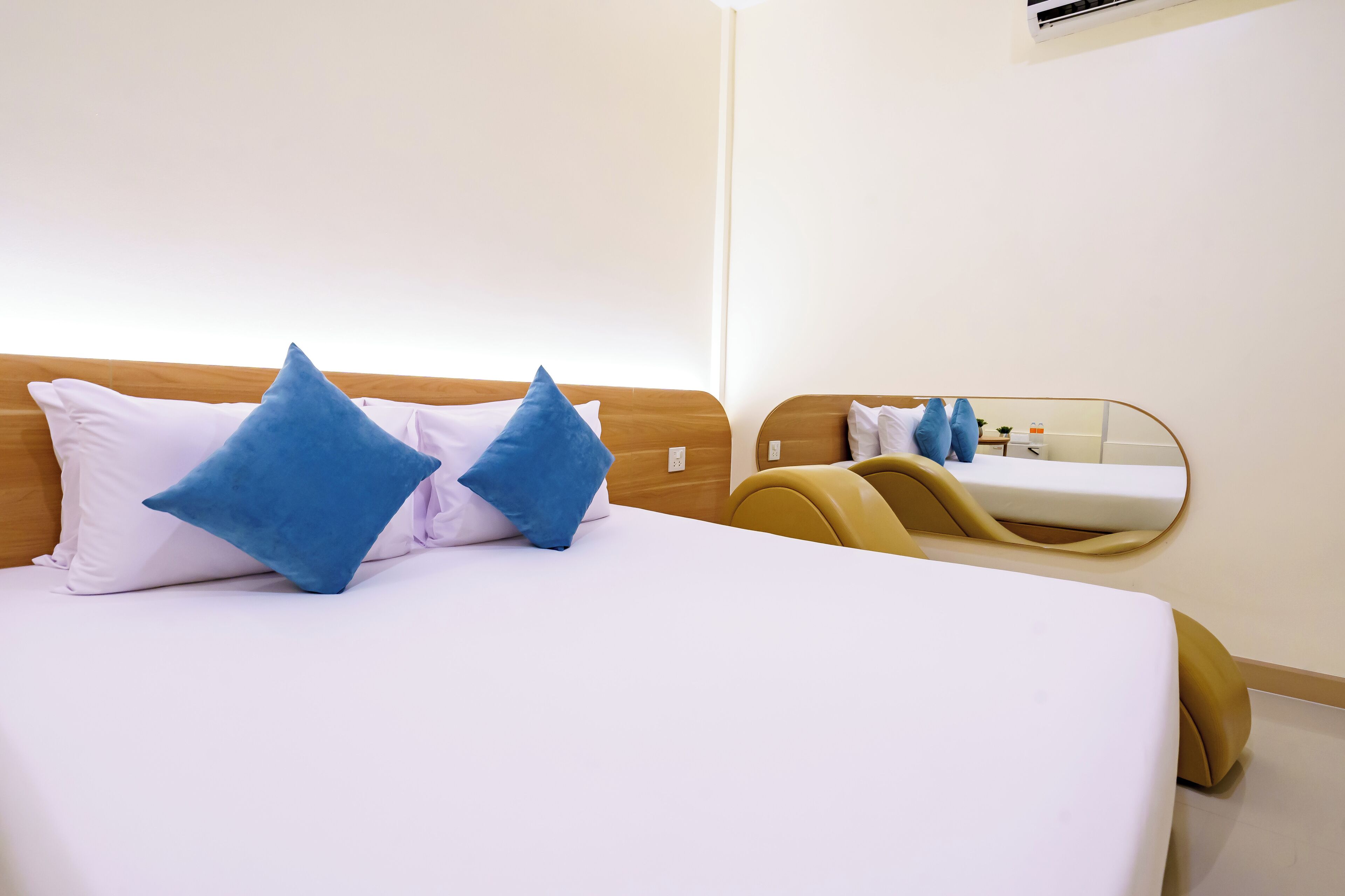 A neatly made bed with white and blue pillows, a wooden headboard, and a mirror on the wall.