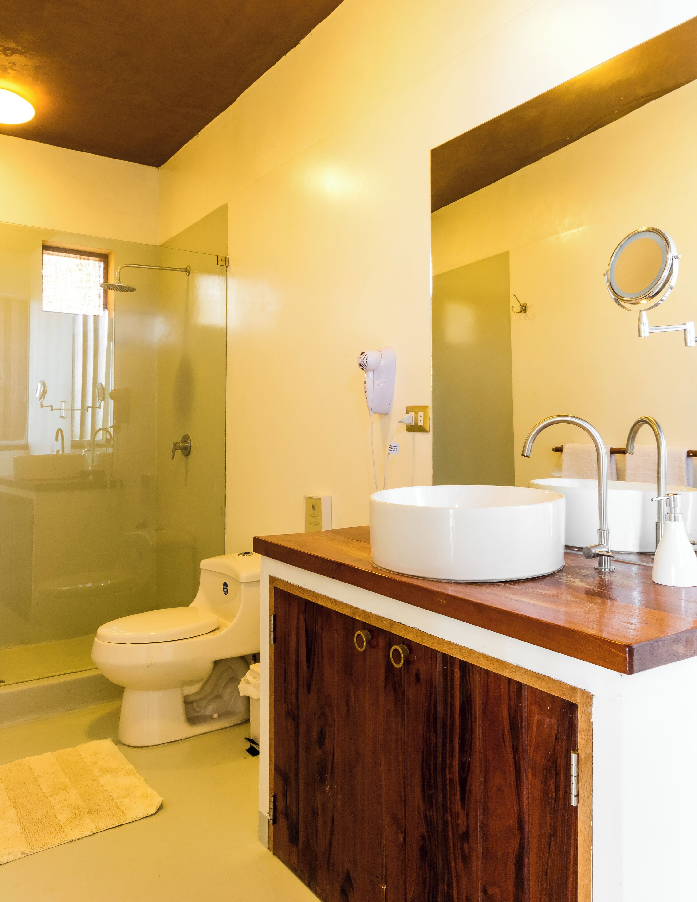 A bathroom with a wooden vanity, a round sink, a toilet, and a glass shower enclosure.