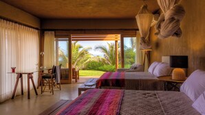 Una habitación con dos camas, zona de comedor y vista a palmeras.