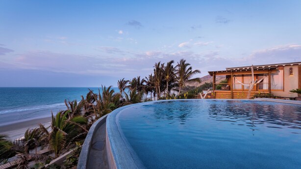 Una piscina con vista a la playa y al océano, rodeada de palmeras y una estructura de madera.