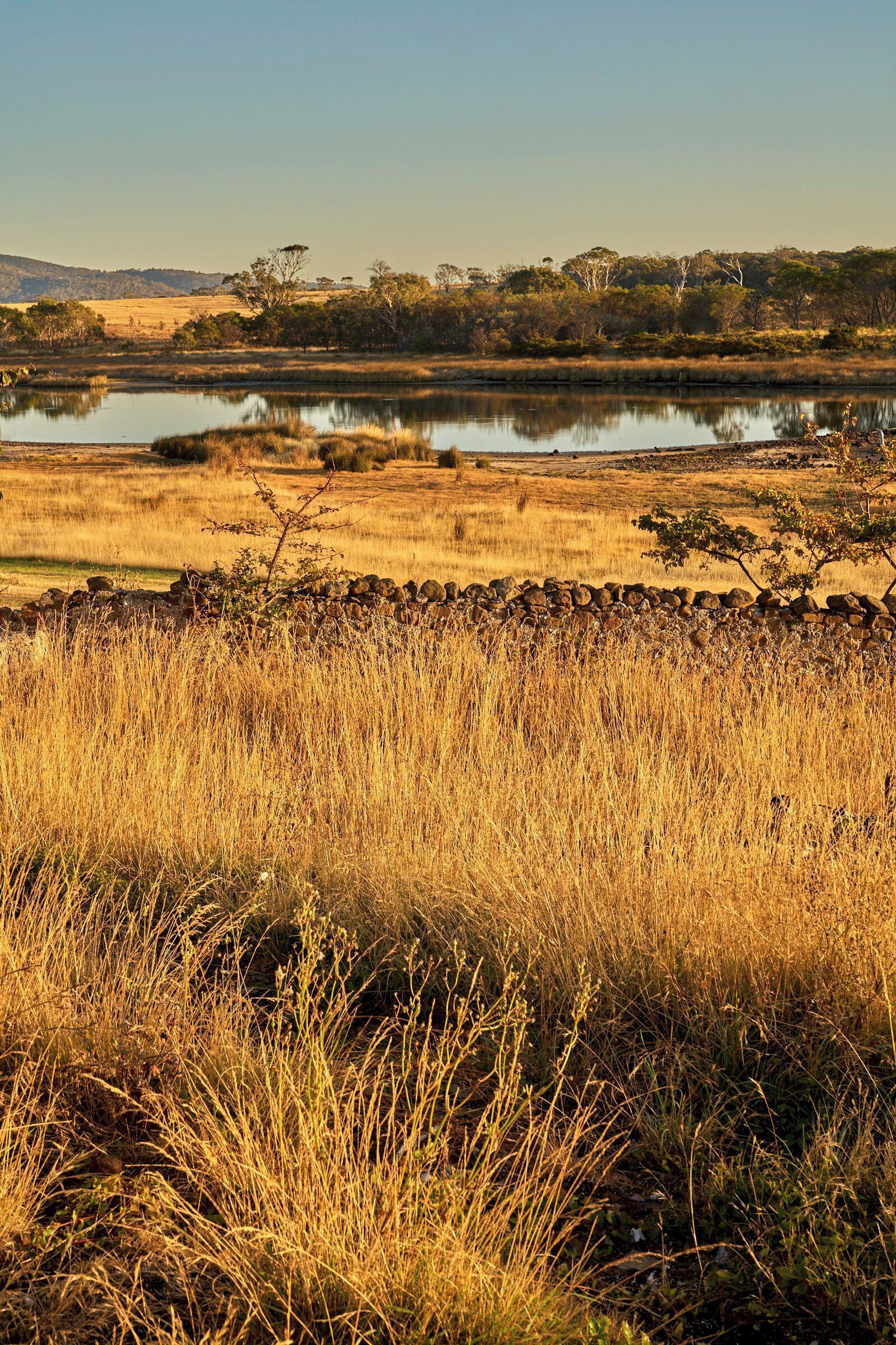 A natural landscape with a body of water, grassy fields, and a stone wall.