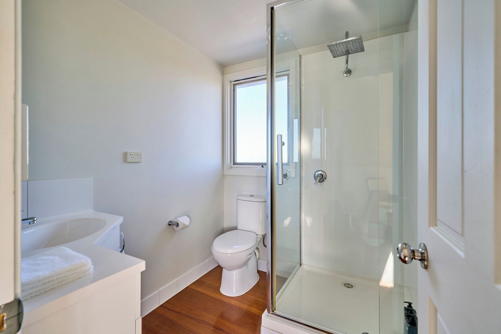 A modern bathroom with a glass shower enclosure, a white toilet, and a sink with a towel.