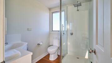 A modern bathroom with a glass shower enclosure, a white toilet, and a sink with a towel.