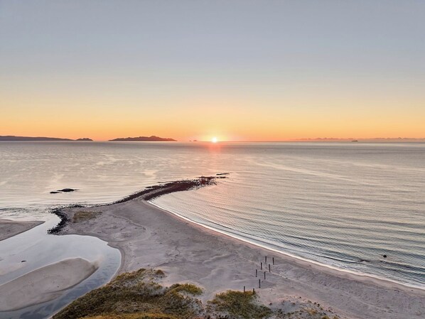 A beach with a clear sky, calm sea, and distant land.