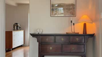 A room with a dark wooden dresser, a white cabinet, a framed picture on the wall, and a table lamp.