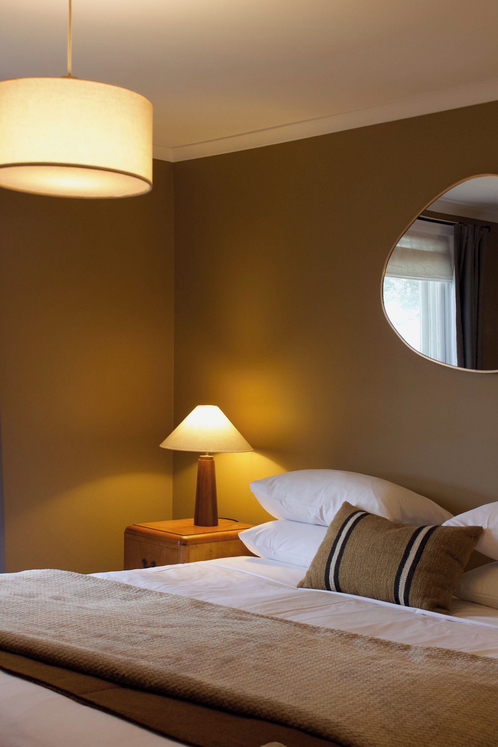 Une chambre d’hôtel avec un lit, une table de chevet, une lampe et un miroir.
