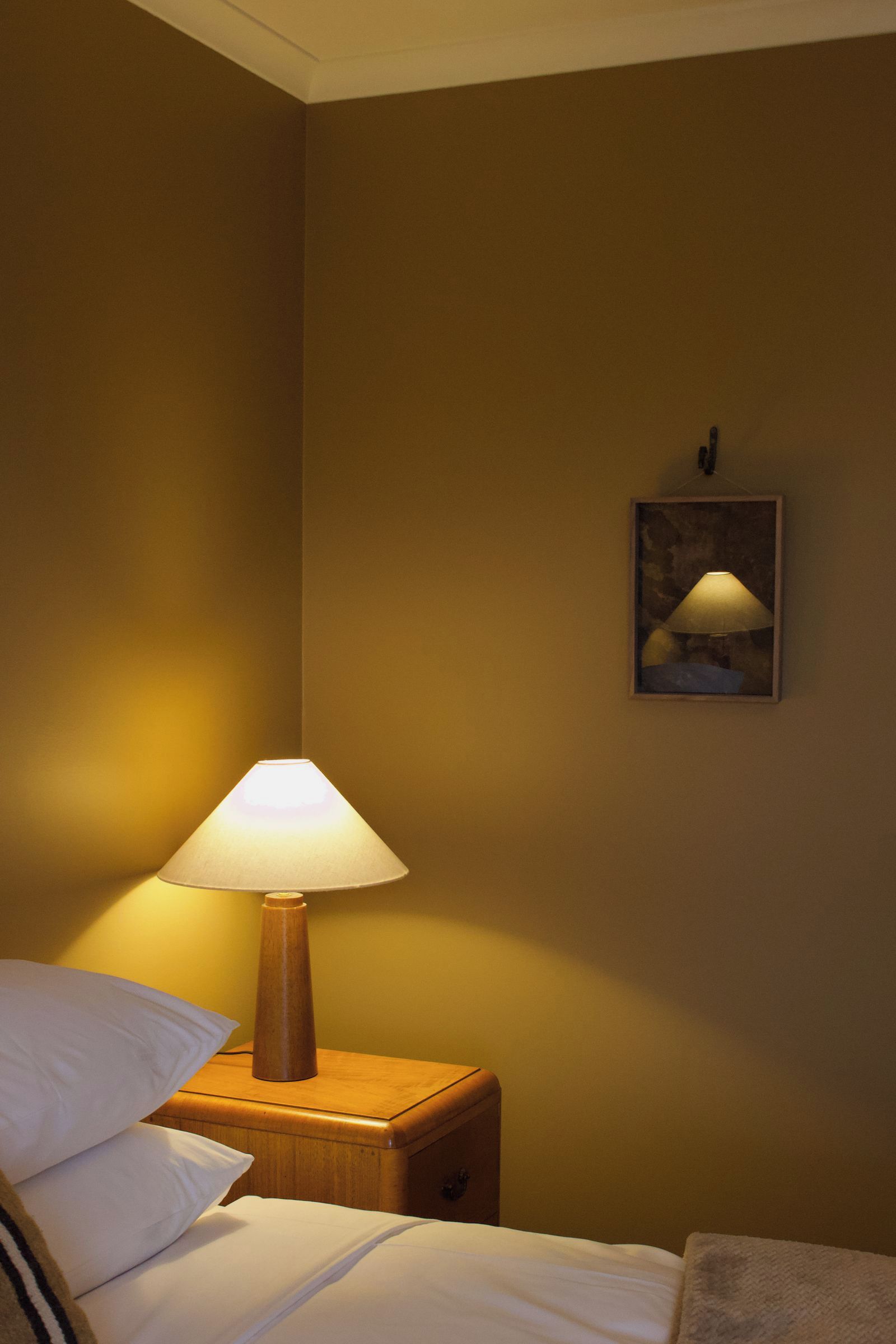 Una habitación de hotel con una cama, una lámpara de noche, una mesita de noche y un cuadro enmarcado en la pared.