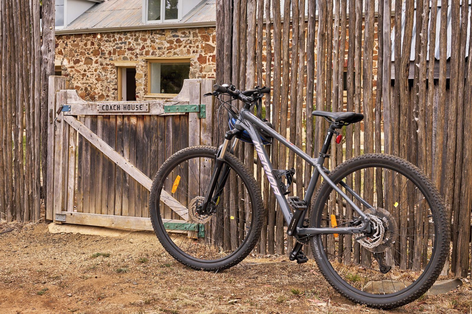 A mountain bike parked in front of a rustic wooden gate labeled 'COACH HOUSE.'