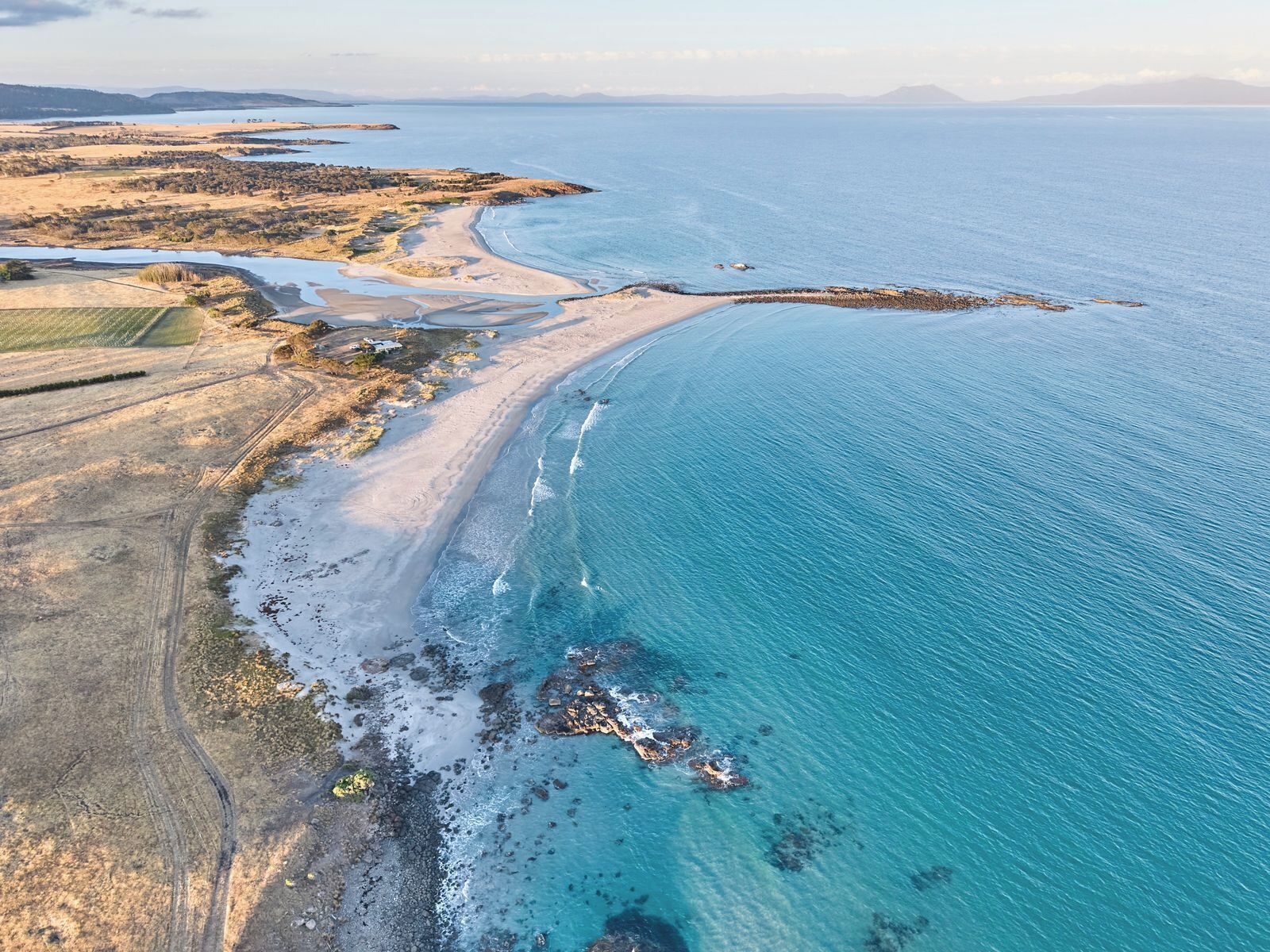 An aerial view of a coastal area with a beach, rocky shoreline, and agricultural fields.