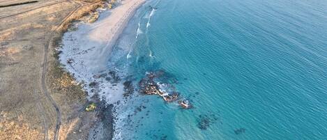 An aerial view of a coastal area with a beach, rocky shoreline, and agricultural fields.