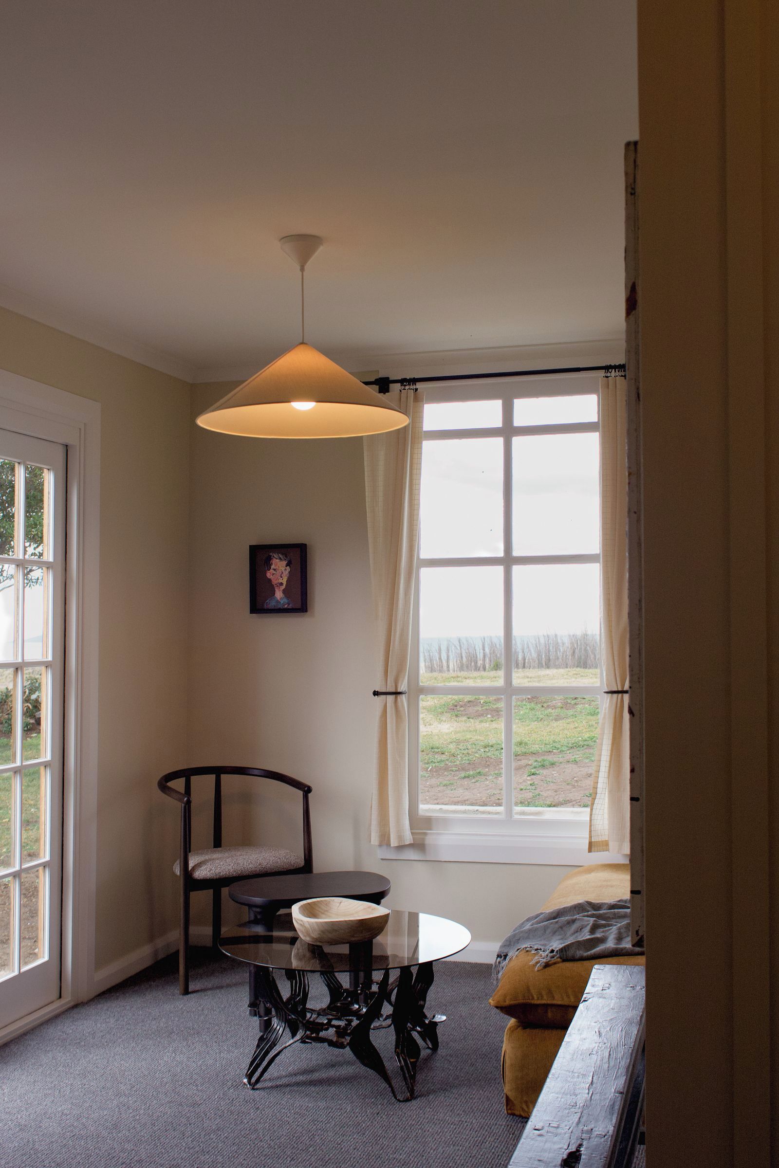 A room with a large window, a chair, a table with a bowl, and a hanging light fixture.