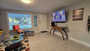 Ein Wohnzimmer mit Fernseher, einem roten Sessel, einem Glastisch und einem Teppich mit Sternfischmuster.