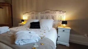 Un letto rifatto con lenzuola bianche e un cuscino nero, due comodini con lampade, e una porta in legno sullo sfondo.