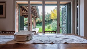 Un'area pranzo con un tavolo apparecchiato per due persone, una ciotola decorativa e vista su un giardino attraverso porte scorrevoli aperte.