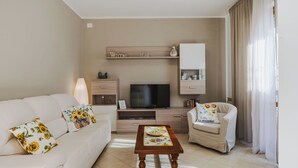 Un salon avec un canapé, un fauteuil, une table basse en bois, une télévision et une pancarte sur laquelle est écrit « Bienvenue à la maison ».