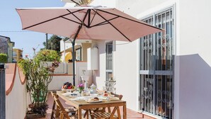 Une terrasse avec une table dressée pour le repas, entourée de plantes en pot et d’un grand parasol.