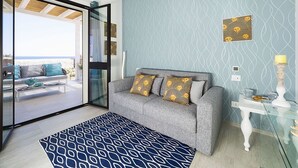 A modern living room with a grey sofa, patterned cushions, a blue rug, and a glass door leading to a balcony with a view of the beach. - Wonderful private villa for 6 people with WIFI, A/C, private pool, TV, terrace and panoramic view (Reitani)