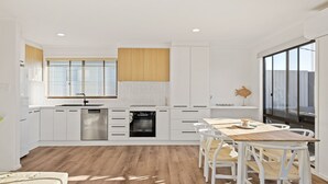 Une cuisine moderne avec des meubles blancs, un plan de travail en bois et un coin repas comprenant une table et des chaises.
