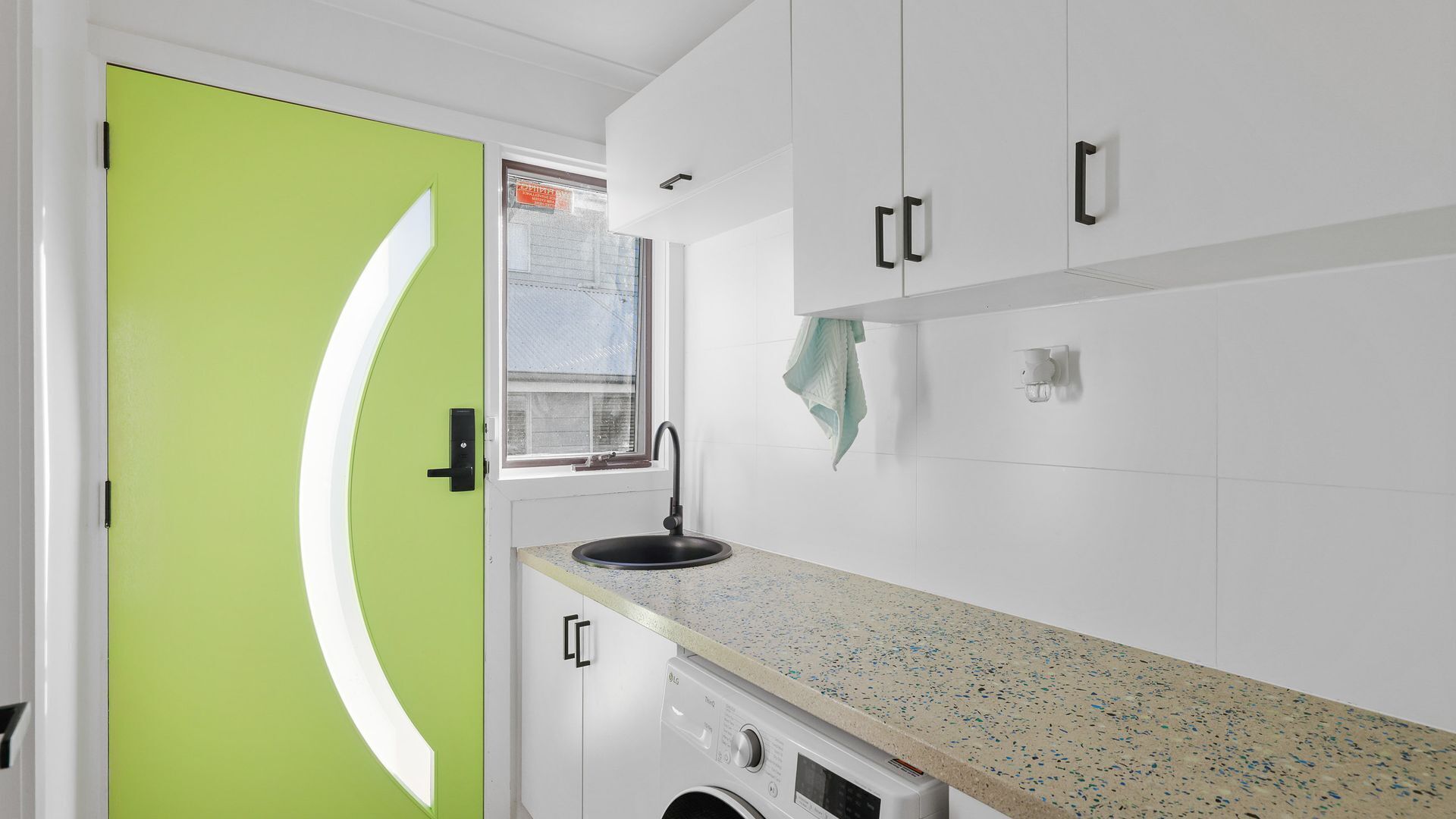 A compact kitchen with a green door, a window, a washing machine, and a sink.