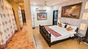 A bedroom with a bed, a nightstand, a wall-mounted air conditioner, a painting, and a patterned floor. - Svarn By Experience Jaisalmer (Jaisalmer)